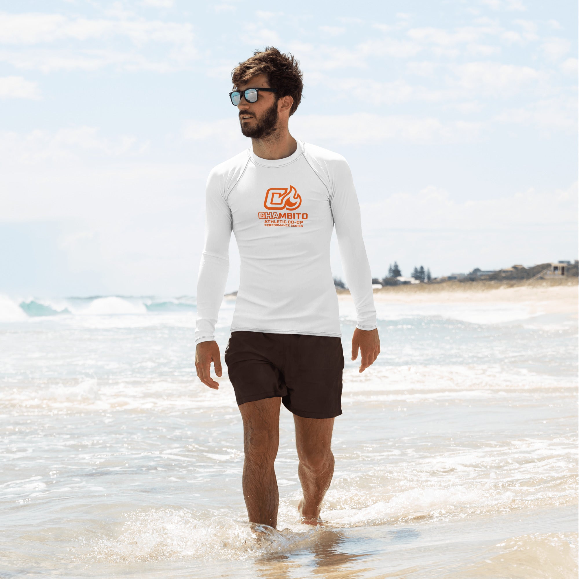 Man wearing a white long-sleeve shirt with text and dark shorts standing on a beach.