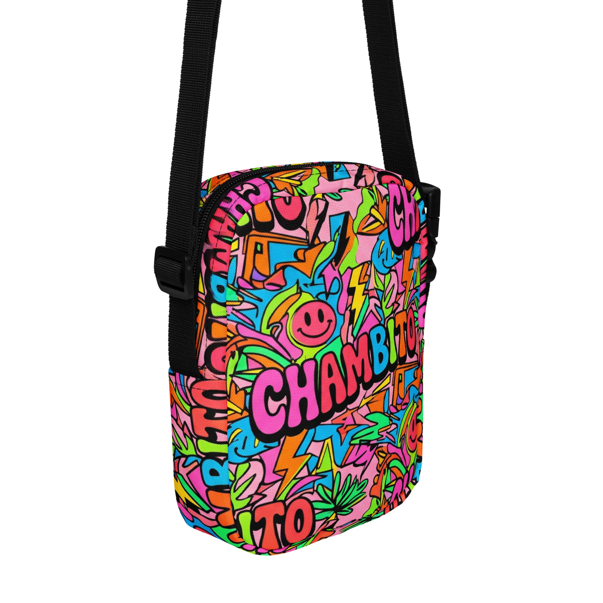 A small crossbody bag with a black adjustable strap, featuring a vibrant, multicolored graffiti-style graphic print with the word 'CHAMBITO' and a smiley face on a plain white background.