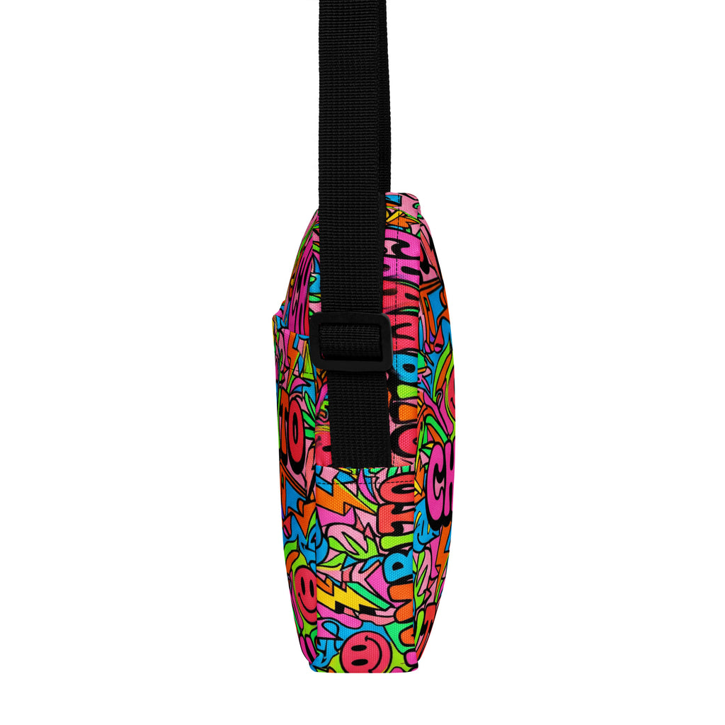 A side view of a shoulder bag featuring a vibrant, multicolored graffiti-style pattern with a black webbed strap and plastic buckle.