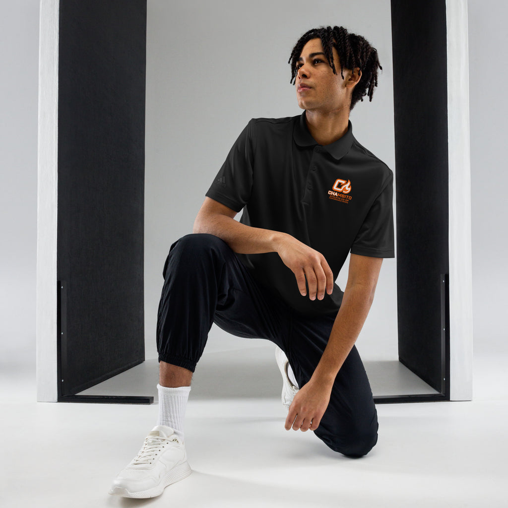 Person wearing a black polo shirt with a logo, sitting on a white stool against a gray background.